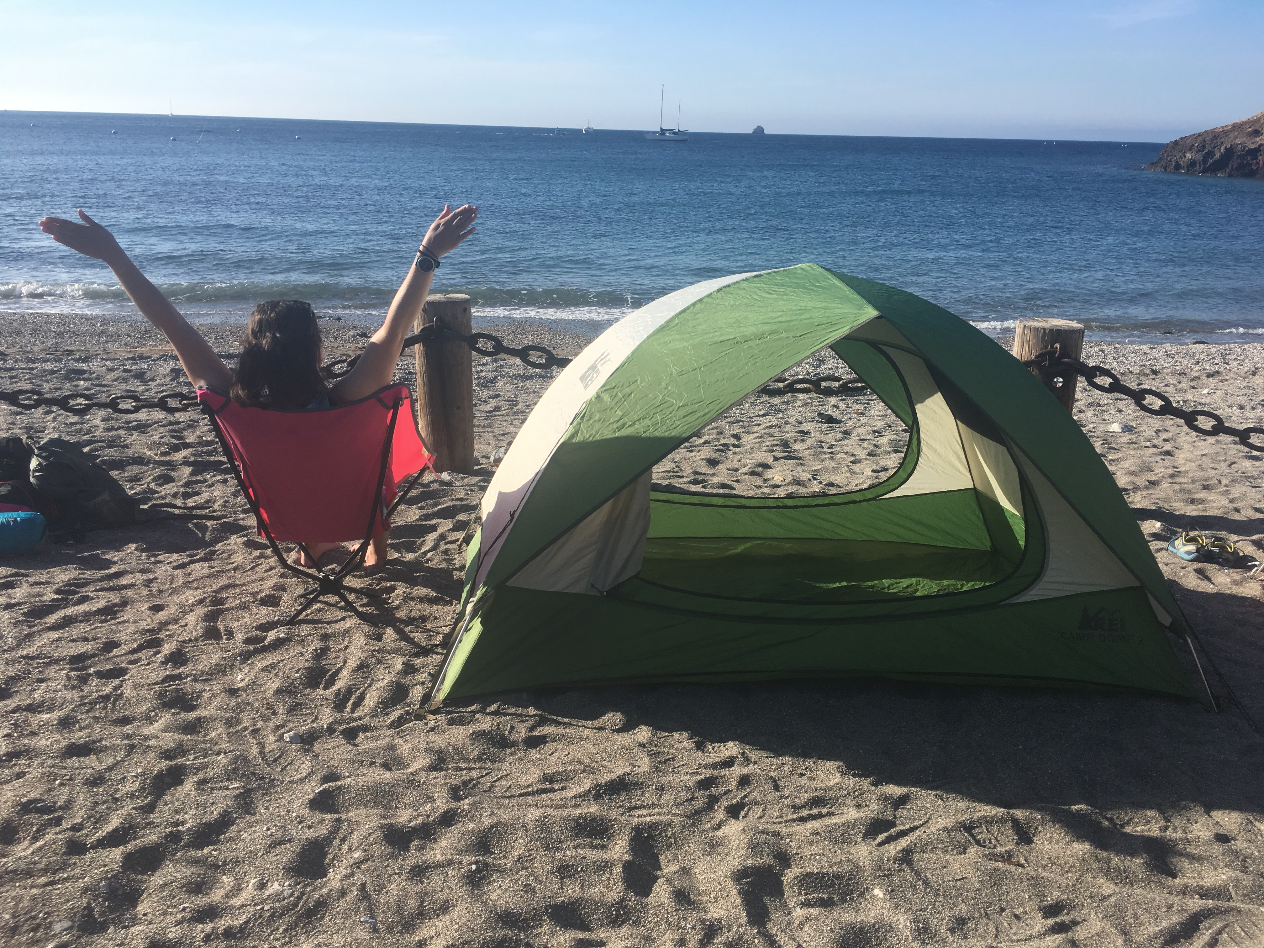 Picture of me sitting in a small pink chair next to my tent facing the ocean